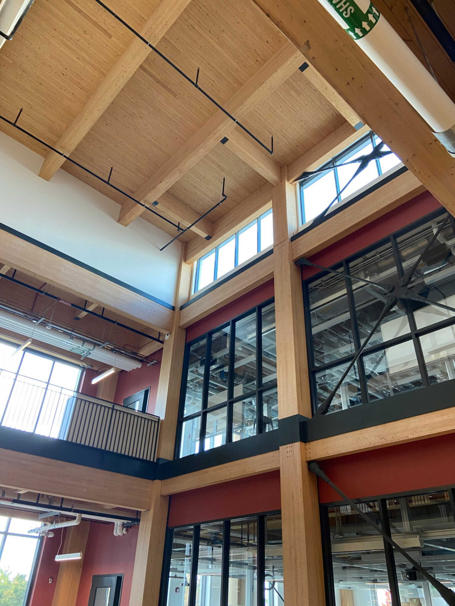 The interior of a building where large wooden beams frame rectangular glass windows.
